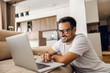 © dusanpetkovic1 - A happy man sits at home and surfs on internet on his laptop.