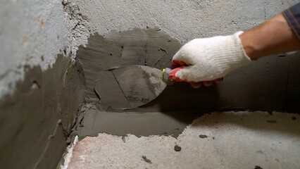 Repairing concrete walls close-up view of the hands of the master. Repair work with a spatula and mortar. builder leveling old bathroom wall with trowel and plaster.