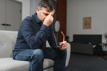 Middle age grey-haired man stressed sitting on sofa at home