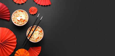 Bowls of tasty Chinese noodles with chopsticks and paper fans on black background with space for text