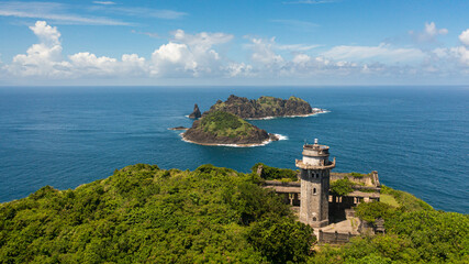 Wall Mural - Lighthouse on a cape against the backdrop of tropical islands and blue sky. Cape Engano. Palaui Island. Santa Ana Philippines.