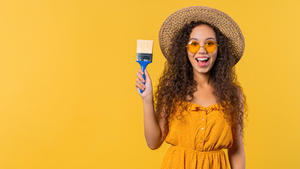 Young curly woman artist with brush on yellow background. Creative person.