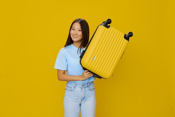 Wall Mural - Asian woman traveling with yellow suitcase and tickets with passport in hand, tourist traveling by plane and train with luggage on yellow background in blue T-shirt and jeans