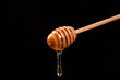 Wooden dipper with honey falling down isolated on black background