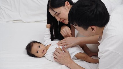 Wall Mural - happy parents (father and mother) talking and playing with baby on a bed