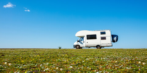 motor home in green meadow against blue sky- travel, vacation, adventure