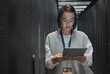 Tablet, server room and cloud computing with a programmer asian woman at work on a mainframe. Software, database and information technology with a female coder working alone on a cyber network