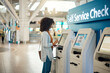© Nina Lawrenson/peopleimages.com - Black woman, airport and self service kiosk for check in, ticket registration or online boarding pass. African female traveler by terminal machine for travel application, document or booking flight