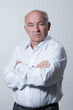 © .shock - Confident senior man in white shirt crossing hands on chest and looking at camera while standing against gray background. Self confident senior isolated white studio shoot.