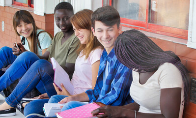 Wall Mural - Multi ethnic schoolmates sitting in the school hallway relaxing and doing school lesson