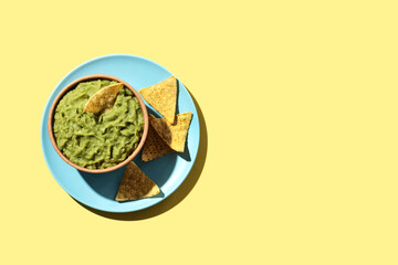 Wall Mural - Mexican guacamole with nacho chip in wooden bowl on yellow background. Top view. Copy space