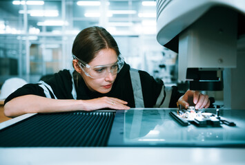 Caucasian female specialist engineer using controller monitor for controlling robotic arm welding machine. Technician maintenance worker in safety uniform working in microchip industry.