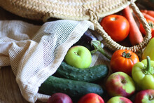 Straw Bag And Reusable Fabric Bags Filled With Various Healthy Fruit And Vegetables. Wooden Background, Selective Focus.