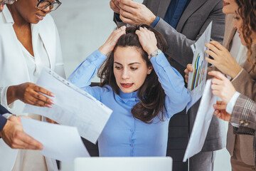 Wall Mural - Frustrated millennial female worker sitting at table with colleagues, felling tired of working quarreling at business meeting. 