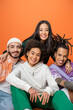 © LIGHTFIELD STUDIOS - happy asian woman embracing stylish multiethnic friends smiling at camera isolated on orange.