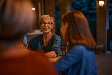 Wall Mural - Happy senior woman talks to her daughter and granddaughter during family dinner on patio.