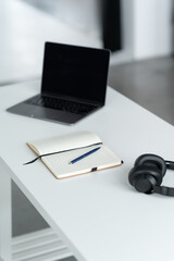 Close-up view of simple workspace with laptop, notebook and headphones