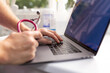 © Austockphoto - Close up shot of a laptop with a healthcare professional using it while holding a stethoscope