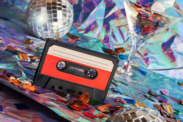 old cassette tape, disco ball and cocktail glass on crumpled neon background.retro and nostalgia style. vintage music, party concept.Y2K design trend