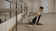 © Framestock - Ballet dancer in training suit near ballet barre stretches legs and practice to performance in dance studio. Beautiful ballerina doing gymnastic exercises and prepares to lesson. Classical ballet art.