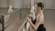 © Framestock - Graceful ballerina in training bodysuit stands near ballet barre, stretches her leg and prepares for performance. Adult woman doing gymnastic exercises in dance studio. Classical ballet dance school.