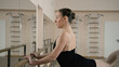 © Framestock - Ballet dancer in training bodysuit stands front of ballet barre in dance studio, stretches leg and prepares for performance. Adult ballerina doing gymnastic exercises. Classical ballet dance school