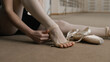 © Framestock - Close up shot of female ballet dancer taking off her pointe shoes after stretching and gymnastic workout in dance studio. Ballerina finished choreography rehearsal. School of classical ballet dance.