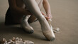 © Framestock - Adult ballerina sits on floor at dance studio and puts on pointe shoes before choreography lesson. Beautiful dancer prepares for performance or training. Classical ballet dance school. Feet close up.