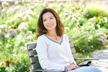 Outdoor portrait of beautiful 40 - 45 years old woman sitting on bench ib green park, healthy lifestyle