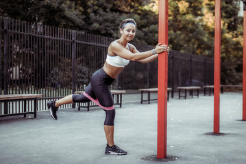 Wall Mural - Young muscular woman trains muscles with fitness rubber bands on a sports workout ground. Healthy lifestyle. Fitness and bodybuilding. Resistance training