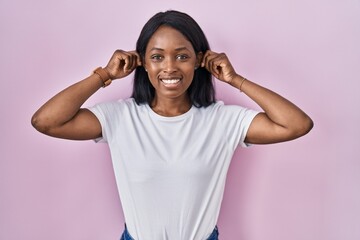 Poster - African young woman wearing casual white t shirt smiling pulling ears with fingers, funny gesture. audition problem