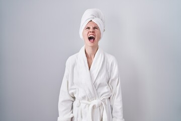 Wall Mural - Blonde caucasian woman wearing bathrobe angry and mad screaming frustrated and furious, shouting with anger. rage and aggressive concept.