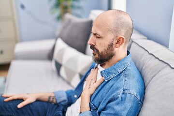 Sticker - Young bald man sitting on sofa suffering heart attack at home