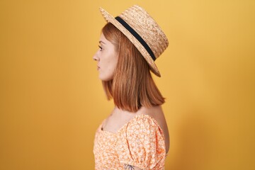 Sticker - Young redhead woman standing over yellow background wearing summer hat looking to side, relax profile pose with natural face with confident smile.