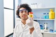 Young hispanic man wearing scientist uniform using laptop analysing urine test tube at laboratory