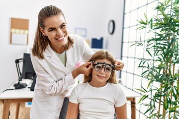 Canvas Print - Woman and girl oculist and patient examining vision using optometrist glasses at clinic