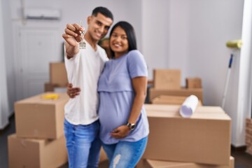 Sticker - Young latin couple expecting baby hugging each other holding key at new home