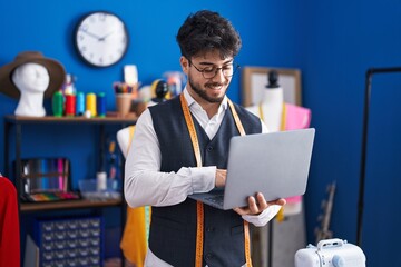 Wall Mural - Young hispanic man tailor smiling confident using laptop at sewing studio