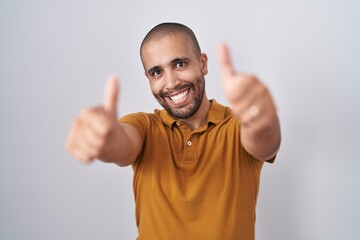 Poster - Hispanic man with beard standing over white background approving doing positive gesture with hand, thumbs up smiling and happy for success. winner gesture.