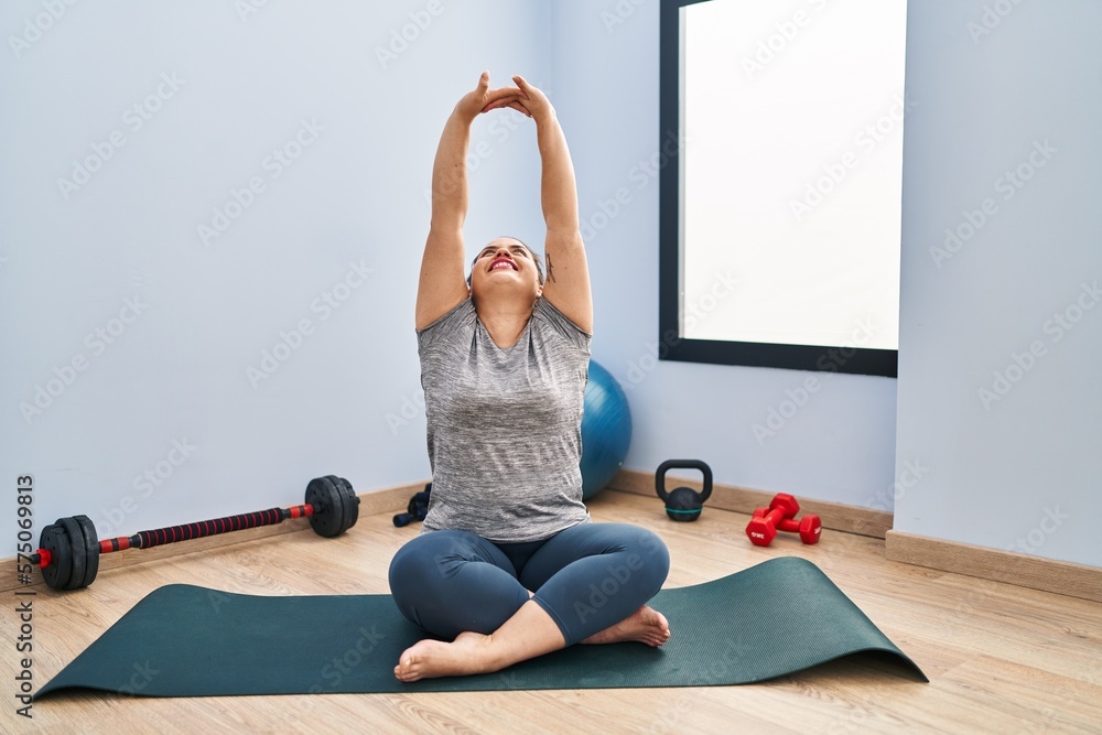 Young beautiful plus size woman smiling confident stretching arms at sport center