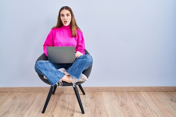 Wall Mural - Young hispanic girl working using computer laptop in shock face, looking skeptical and sarcastic, surprised with open mouth