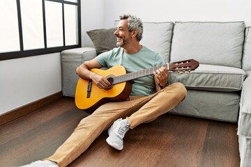 Sticker - Middle age grey-haired man playing classical guitar sitting on floor at home