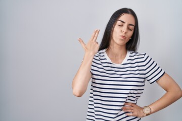 Sticker - Young brunette woman wearing striped t shirt shooting and killing oneself pointing hand and fingers to head like gun, suicide gesture.