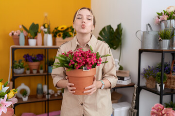 Poster - Young caucasian woman working at florist shop holding plant pot looking at the camera blowing a kiss being lovely and sexy. love expression.