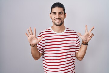 Wall Mural - Hispanic man with long hair standing over isolated background showing and pointing up with fingers number eight while smiling confident and happy.