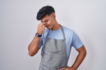 Poster - Hispanic young man wearing apron over white background tired rubbing nose and eyes feeling fatigue and headache. stress and frustration concept.