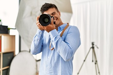 Wall Mural - Young hispanic man photographer using professional camera at photography studio