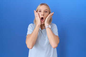 Wall Mural - Young caucasian woman wearing casual blue t shirt afraid and shocked, surprise and amazed expression with hands on face