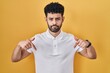 © Krakenimages.com - Arab man standing over yellow background pointing down looking sad and upset, indicating direction with fingers, unhappy and depressed.