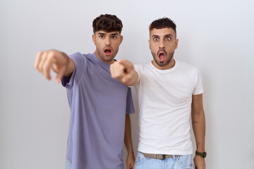 Canvas Print - Homosexual gay couple standing over white background pointing with finger surprised ahead, open mouth amazed expression, something on the front